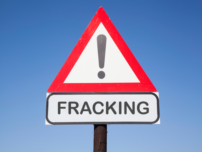Warnschild mit Ausrufezeichen und dem Schriftzug "Fracking" vor blauem Hintergrund.