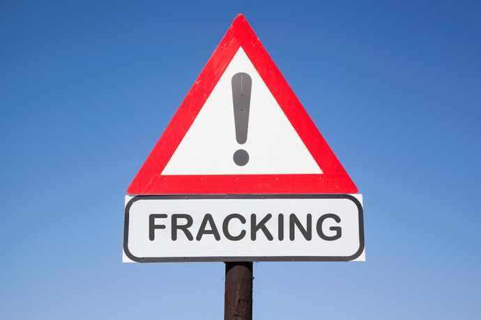 Warnschild mit Ausrufezeichen und dem Schriftzug "Fracking" vor blauem Hintergrund.