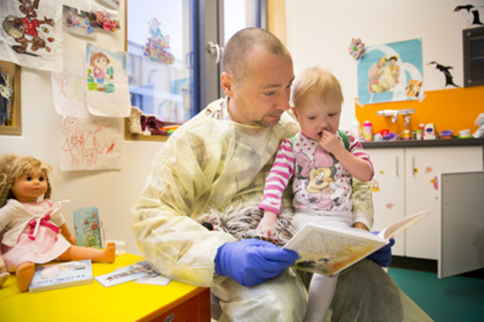 Foto eines Mitglieds von mitMenschen, das einem Kleinkind in einem Krankenhaus etwas vorliest