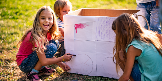 Draußen spielende Kinder, die einen Karton bemalen