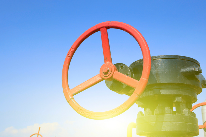 Rotes Handrad einer Industriearmatur an einer Pipeline vor blauem Himmel.
