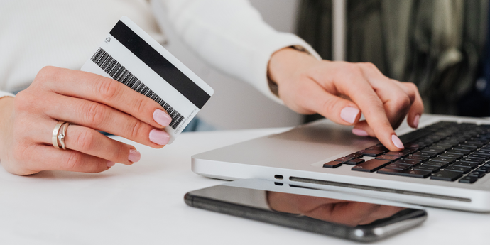 Hand hält Kreditkarte und tippt auf Laptop bei einer Online-Zahlung, Smartphone liegt daneben
